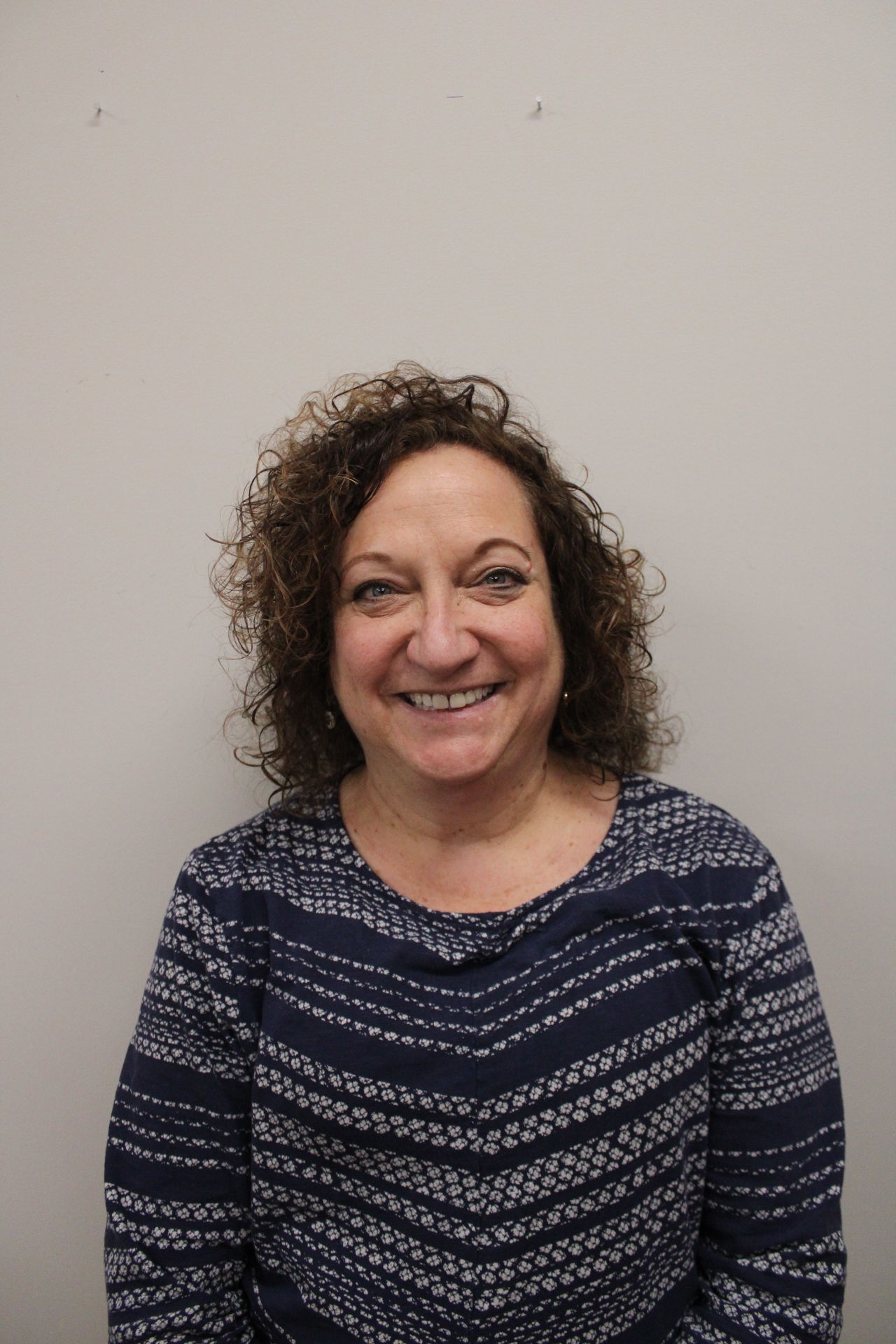 Smiling woman with curly hair against plain wall