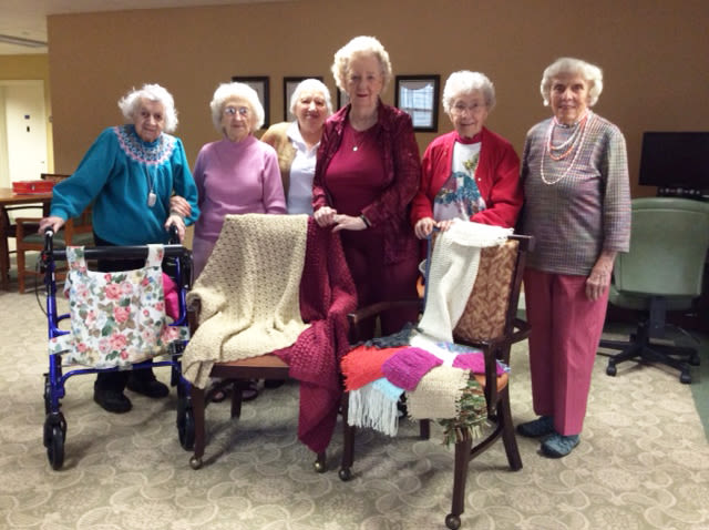 Six elderly women displaying handmade knitted blankets