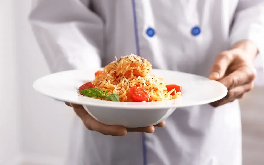 Chef presenting spaghetti with cherry tomatoes and basil