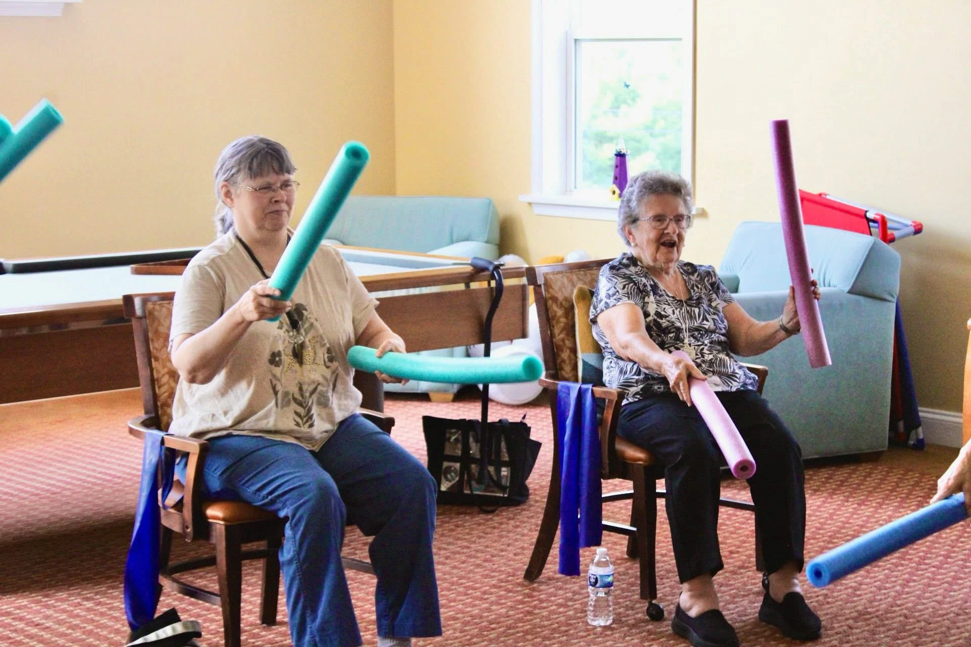 Two seniors exercising with pool noodles indoors